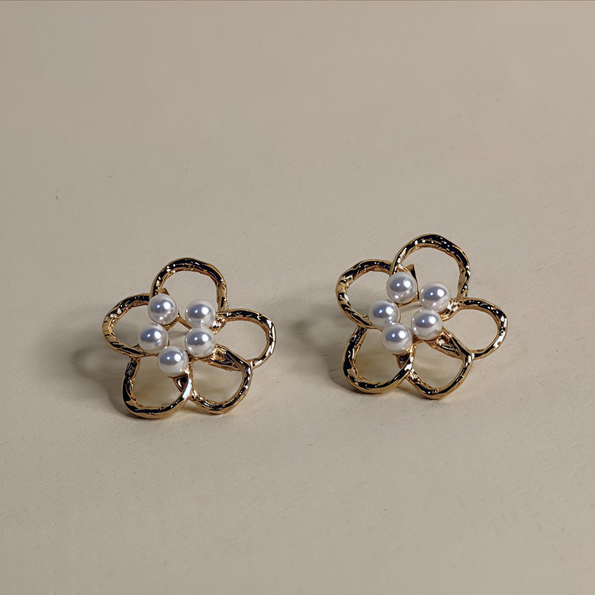 Pair of flower-shaped earrings with pearl centers on a beige background