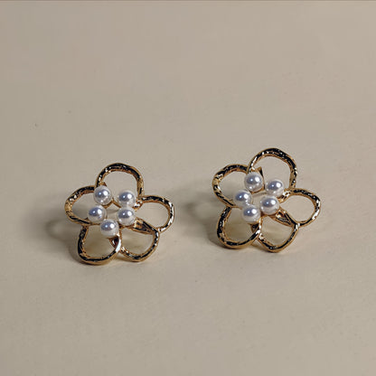Pair of flower-shaped earrings with pearl centers on a beige background