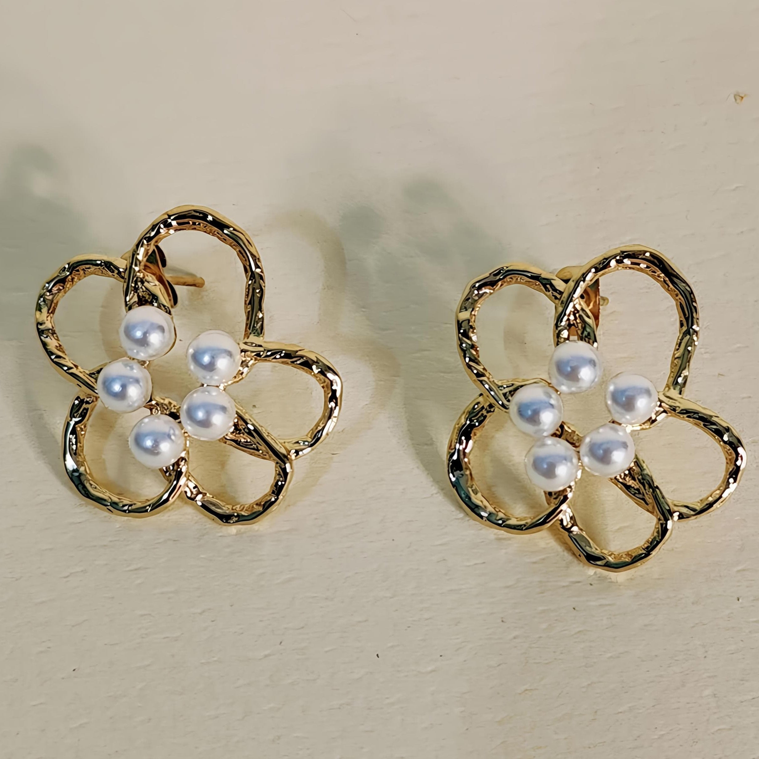 Gold flower-shaped earrings with pearl centers on a beige background