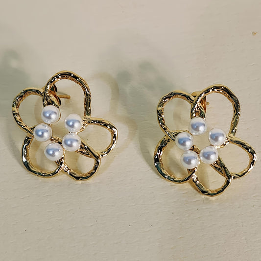 Gold flower-shaped earrings with pearl centers on a beige background