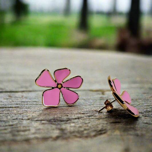 Pink flower-shaped earrings with gold accents on a beige background
