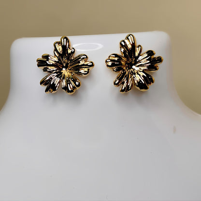 Gold floral earrings on a mannequin bust against a beige background