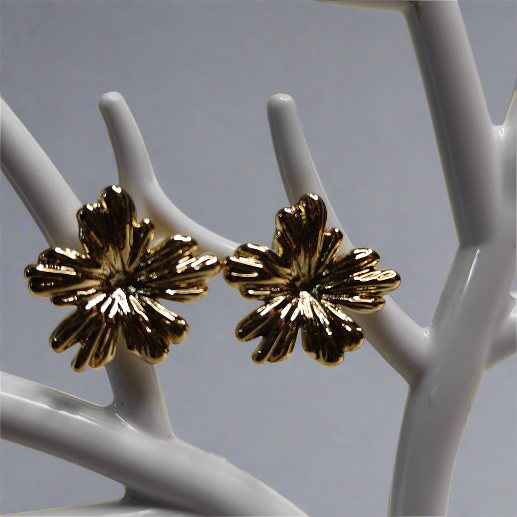 Gold floral earrings on a white stand against a beige background