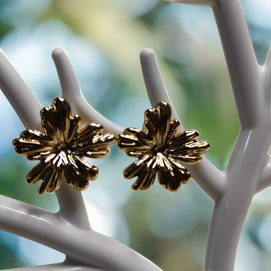 Gold floral earrings on a white stand against a beige background