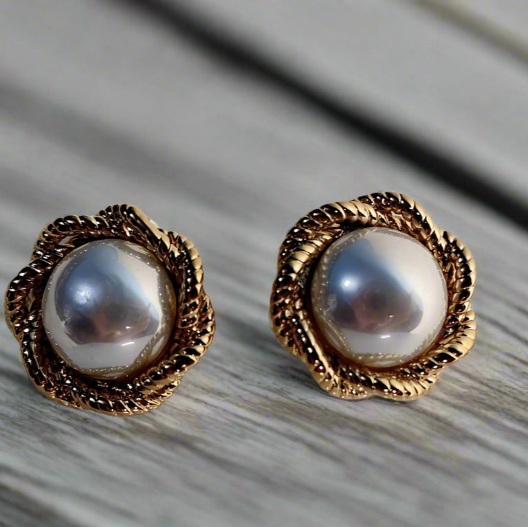 Pair of pearl earrings with gold accents on a white stand against a beige background