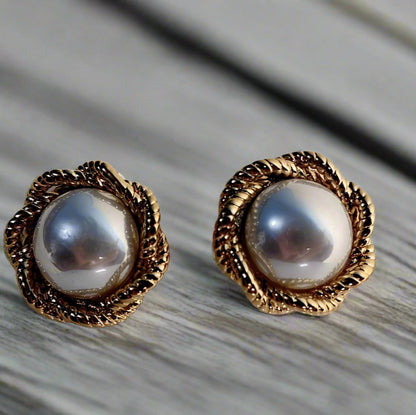 Pair of pearl earrings with gold accents on a white stand against a beige background